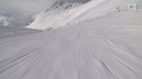 Ripresa in soggettiva di uno sciatore che percorre a tutta velocità una pista da sci; in lontananza, skilift