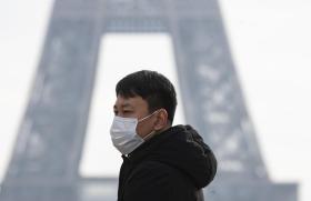Un turista asiatico con la mascherina ai piedi della Tour Eiffel di Parigi