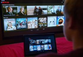 Un ragazzo davanti a diversi schermi con le offerte di serie televisive di Netflix