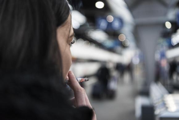 Donna, di schiena, fuma una sigaretta mentre osserva una banchina ferroviaria (sfocata)