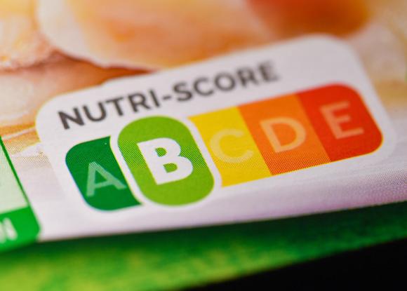 Primissimo piano di etichetta di un prodotto alimentare, con un logo A-B-C-D-E di cui è evidenziata la B in colore verde chiaro