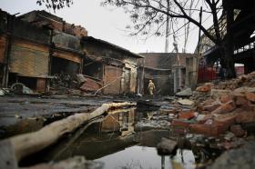 Immagine di un quartiere sterrato, con negozi con serrande semi-alzate e interni bruciati, e detriti sulla strada