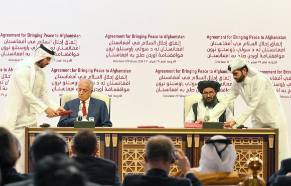 Uomo in abiti occidentali e altro in abiti mediorientali si apprestano a firmare un documento; scritte in arabo sul fondo