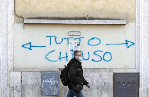 uomo cammina davanti a un graffiti con la scritta tutto chiuso