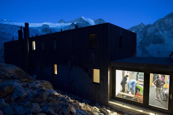 Paesaggio alpino ripreso di notte con, in primo piano, una costruzione squadrata; si intravvedono persone all interno