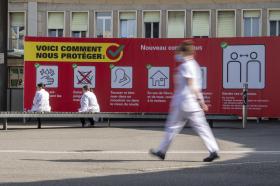 Davanti all ospedale universitario di Ginevra personale sanitario passa davanti ai cartelloni che indicano come proteggersi.