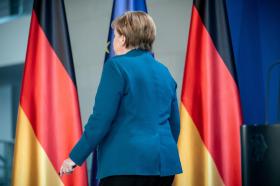 Angela Merkel ripresa di spalle con sullo sfondo le bandiere tedesche.