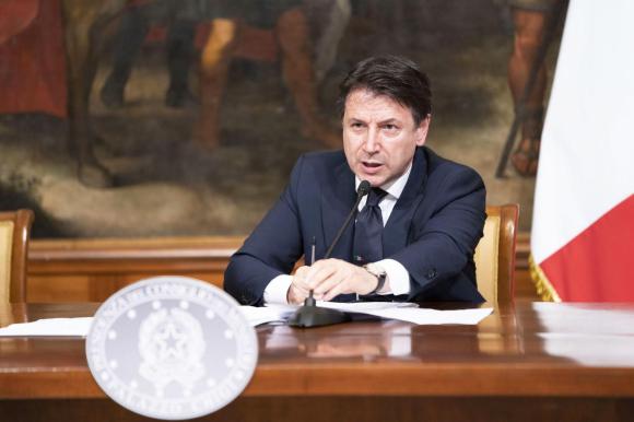 Il premier italiano a un tavolo con l emblema della Presidenza del Consiglio dei ministri e una bandiera italiana accanto