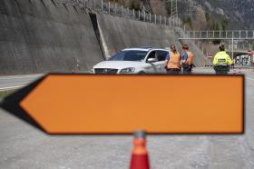 Primo piano (sfocato) di un cartello arancione da deviazione stradale - dietro due poliziotte urane e una ticinese fermano auto