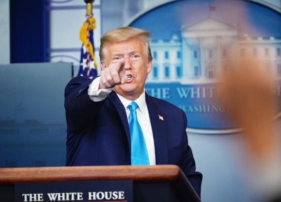 Trump indica qualcuno con l indice (forse un giornalista cui dà parola) da un pulpito; dietro di lui stemma della Casa Bianca