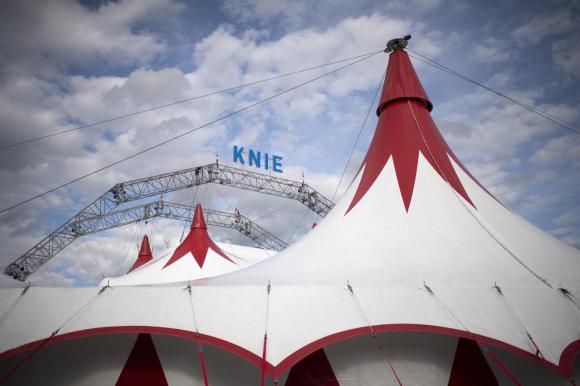 Tendone di circo con scritta Knie visto dal basso; il cielo sovrastante è nuvoloso.