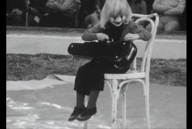 Bambino vestito da clown seduto in un arena da circo con la custodia di uno strumento musicale sulle ginocchia