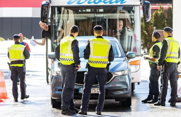 Cinque uomini con gilet rilfettente con scritta Polizei controllano un auto e un autobus in un valico di frontiera