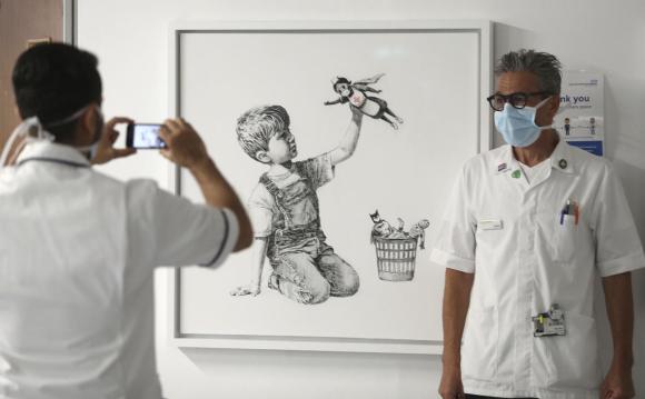Un medico on mascherina posa davanti all opera di Banksy