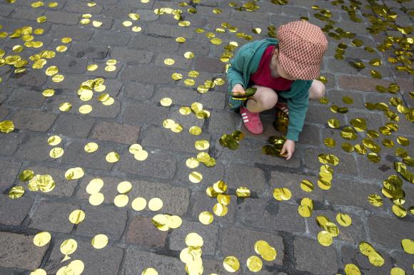 un bambino raccoglie coriandoli dorati in strada.