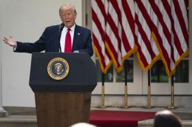 Donald Trump parla dal pulpito presidenziale nel giardino della Casa Bianca; fa un gesto distensivo
