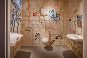 Un bagno pubblico (finto, ricostruito in un museo), con tag e battute scritte sulle pareti