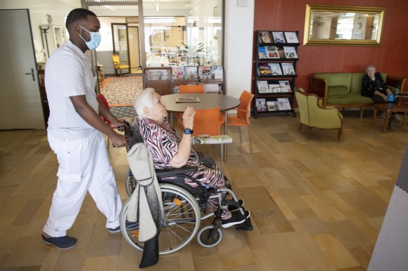 infermiere spinge la carrozzella su cui è seduta un anziana