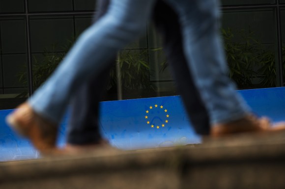Persone camminano davanti a barriera con logo UE