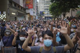 Migliaia di persone in corteo in una strada metropolitana; quasi tutti con mani alzate; tutti indossano mascherina