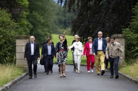 Gruppo di uomini e donne, vestiti piuttosto casual, passano accanto a colonne sul vialetto di un parco
