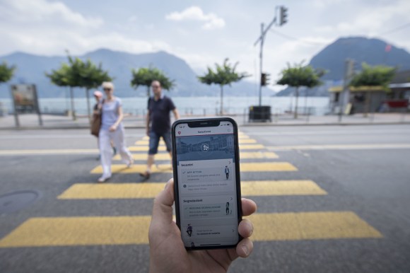 UN telefonino con l app swisscovid e sullo sfondo la baia di Lugano