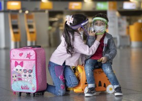 UN^na bimba aiuta un bambino a mettere correttamente la mascherina all aeroporto di Francoforte