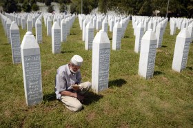 Un uomo prega in ginocchio in mezzo alle tombe del cimitero dedicato alle vittime di Srebrenica.