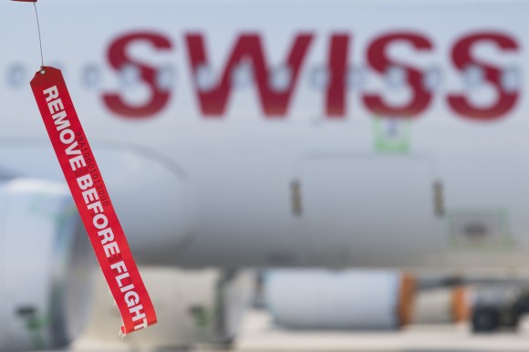 Fusoliera di aereo Swiss vista sfuocata; in primo piano, a fuoco, linguetta con scritta Remove Before Flight