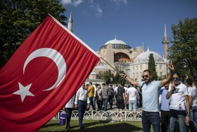 un uomo sventola un enorme bandiera turca davanti alla basilica di Santa Sofia.