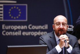 Michel seduto davanti a un microfono con le mani conserte come in preghiera; dietro, logo del Consiglio UE