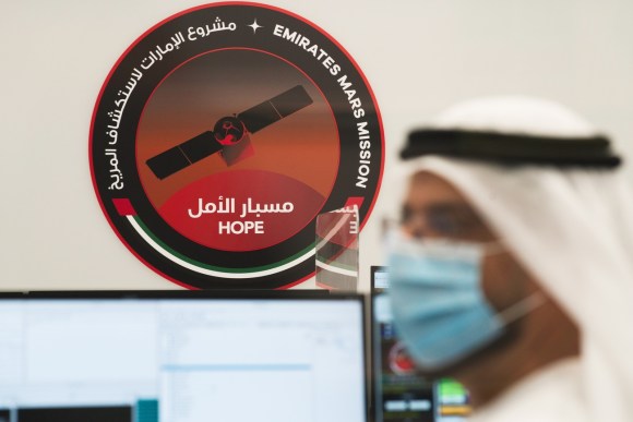 Logo circolare di satellite su sfondo rosso con scritte (in arabo e inglese) Emir. ar. uniti e Speranza ; si intravvede uomo