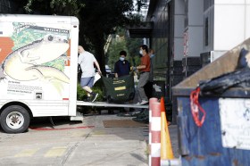 Due uomini portano caricano su un furgone una sacca verde con scritto Diplomatic bag sul retro di un edificio
