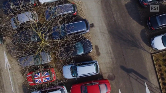 Parcheggio fotografato da un drone; auto di vario colore, piante e aiuole