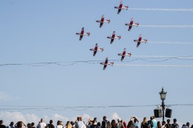 Una folla guarda verso il cielo una squadriglia di PC-7 si esibisce in voli acrobatici.