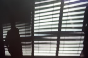 Silhouette di una persona vista in controluce e dietro le lamelle di una tapparella