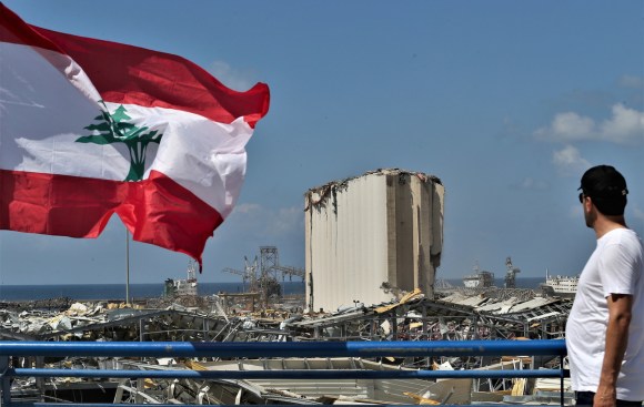 La zona del porto di Beirut devastata dalle esplosioni e in primo piano la bandiera libanese.