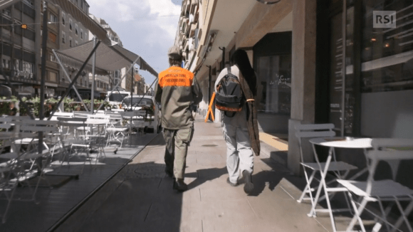 Due persone, di cui una con tuta protezione civile e l altra con zainetto, camminano per strada di città