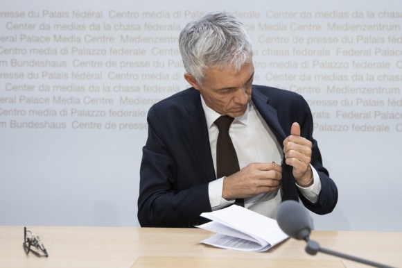Uomo in abiti formali rimette la penna nella tasca interna della giacca prima di alzarsi da tavolo di conferenza stampa