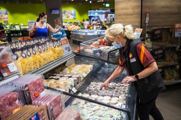 Reparto formaggi salumi di un supermercato; commessa e clienti indossano mascherina
