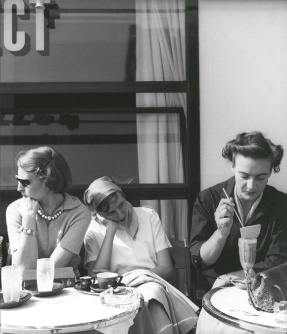 tre donne sedute a due tavolini di un caffè.