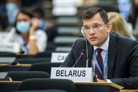 Uomo in abito formale con apparecchio per la traduzione e cartellino Belarus seduto in un emiciclo