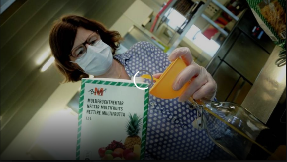 Donna con mascherina travasa del succo multifrutta da un tetrapack a una bottiglia in un laboratorio