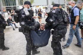 Due poliziotti in tenuta antisommossa trascinano via, tenendolo per gambe e braccia, una persona da un raduno