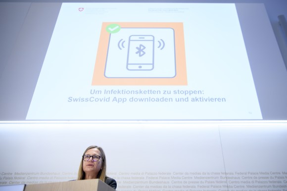 Donna parla da un pulpito; alle sue spalle un immagine invita a scaricare l app SwissCovid
