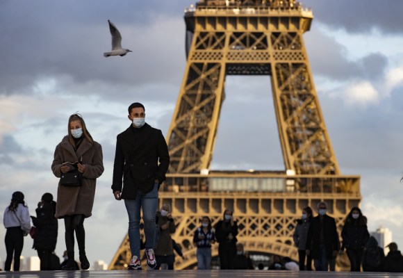 Turisti, tutti con mascherina, passeggiano nei pressi della Tour Eiffel di Parigi, sul fondo, sfocata al crepuscolo