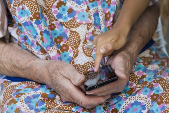 un anziana tiene in mano uno smartphone e qualcuno le mostra il funzionamento.