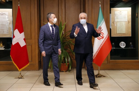 Due uomini in piedi tra il vessillo svizzero e quello iraniano.