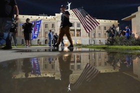 Manifestanti con bandiere USA o Trump-Pence di notte davanti a costruzione neoclassica