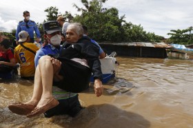 Poliziotto con l acqua fino alla cintola in un area tropicale alluvionata porta in braccio una donna anziana